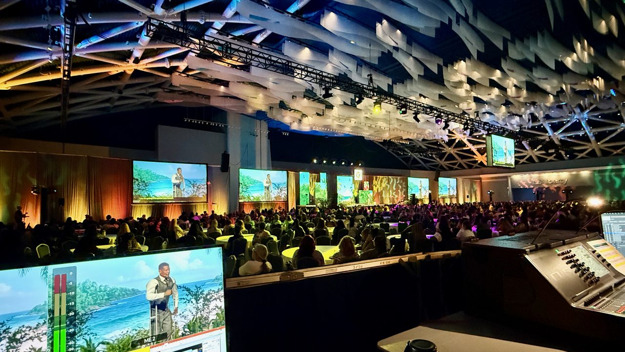 Production desk view of tropical-themed conference with multiple LED panels