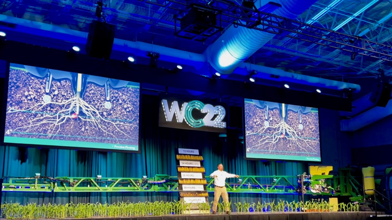 Agricultural conference with speaker on stage and crop science graphics